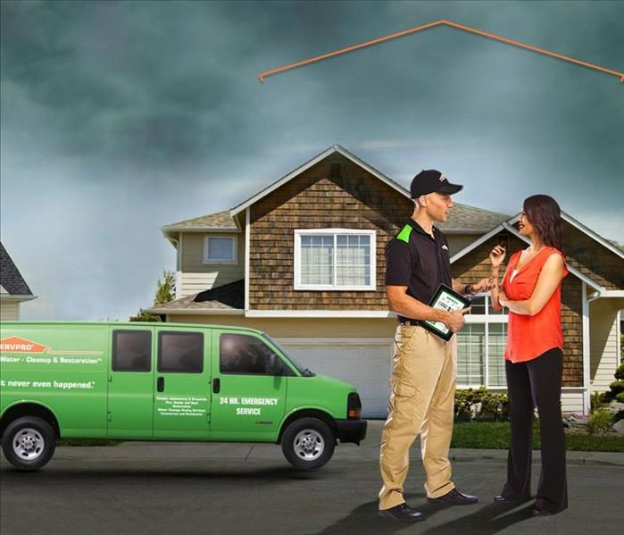 Green SERVPRO vehicle outside of residential home with storm clouds in the sky. A man and woman stand outside talking.