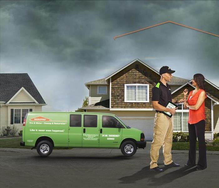 Servpro technician standing outside home explaining next steps with homeowner with two homes and a Servpro van behind them.